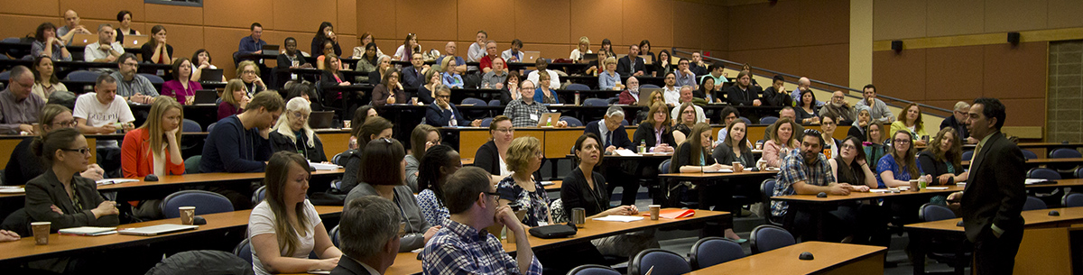 A speaker presenting to a lecture theatre full of attendees.