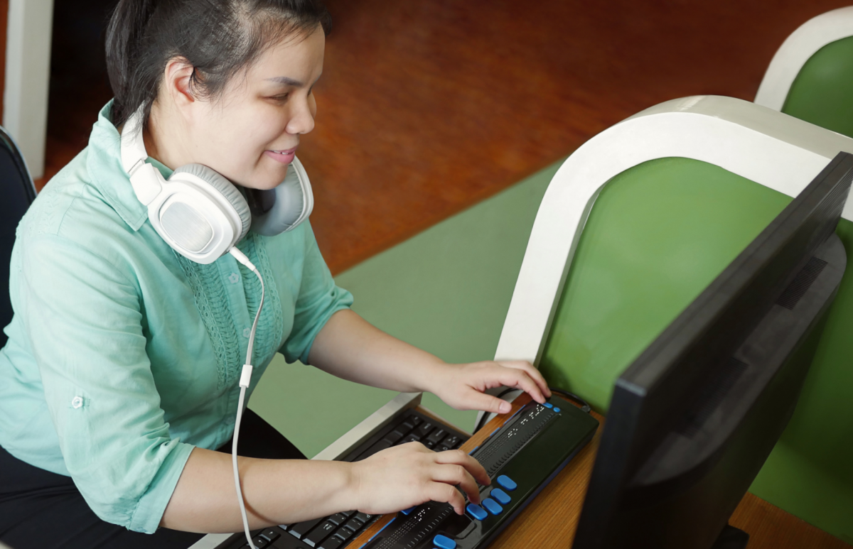 A picture of a Blind woman using a computer with refreshable braille display.